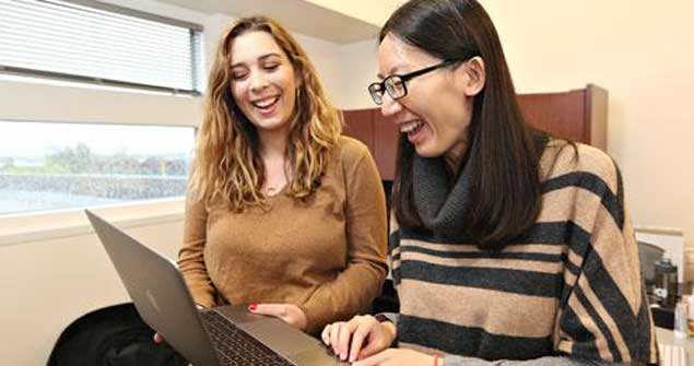 Two women looking at their laptops while smiling