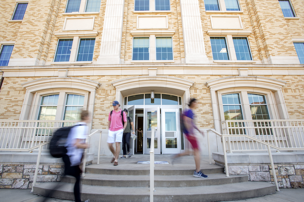 Students wave at the camera as they walk along the Campus Commons