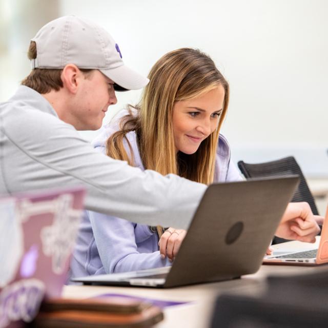 Two students work together on a laptop computer